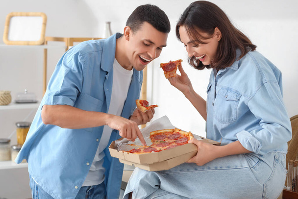 Jong stel dat lekkere pepperoni pizza eet in de keuken - Foto, afbeelding