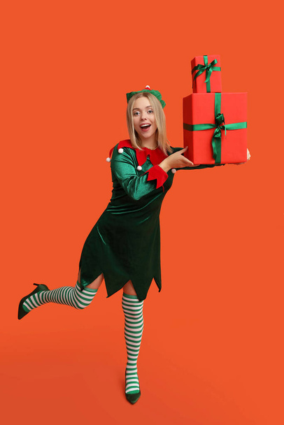 Эмоциональная девушка в костюме эльфа с рождественскими подарочными коробками на оранжевом фоне - Фото, изображение