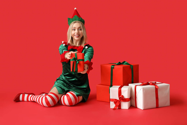Счастливая девушка в костюме эльфа с рождественскими подарочными коробками на красном фоне - Фото, изображение