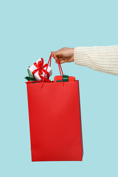Γυναίκα κρατώντας τσάντα αγορών με κουτιά δώρο Χριστουγέννων σε μπλε φόντο - Φωτογραφία, εικόνα