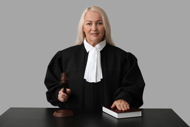 Mature female judge with gavel and book at table on grey background - Photo, Image