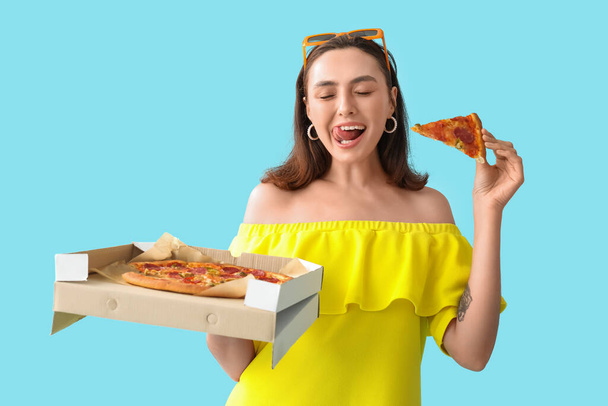 青い背景においしいピザとダンボール箱を保持している若い女性 - 写真・画像