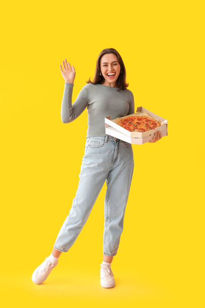 Jovem segurando caixa de papelão com pizza saborosa no fundo amarelo - Foto, Imagem