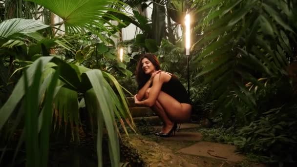 Szexi nő fekete öltönyben pózol egy trópusi kertben. Fogalom a divat fotózás. 4k - Felvétel, videó