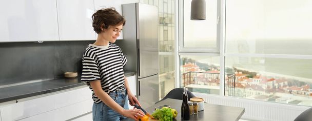 Retrato de una joven cocinando ensalada. Linda chica vegana cortar verduras en el mostrador de la cocina, la preparación de alimentos. - Foto, Imagen