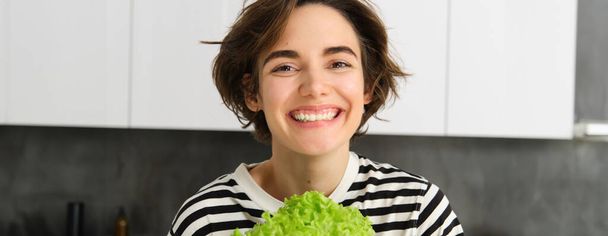 Close up portrait of beautiful, healthy smiling woman, posing with green lettuce leaf, cooking diet meal, preparing vegetarian salad, looking happy. - Foto, Imagen
