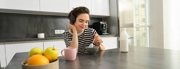 Portrait du matin d'une femme souriante prenant son petit déjeuner, tenant une cuillère, prenant des céréales avec du lait et buvant du café. - Photo, image