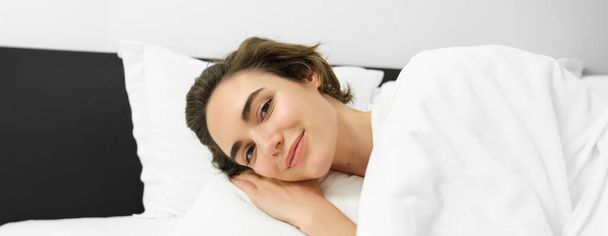 Gülümseyen genç bir kadının yakın portresi, dinleniyor, sakin bir şekilde yatakta uzanıyor, hassas bir yüz ifadesi, dinleniyor, uykuya dalıyor.. - Fotoğraf, Görsel