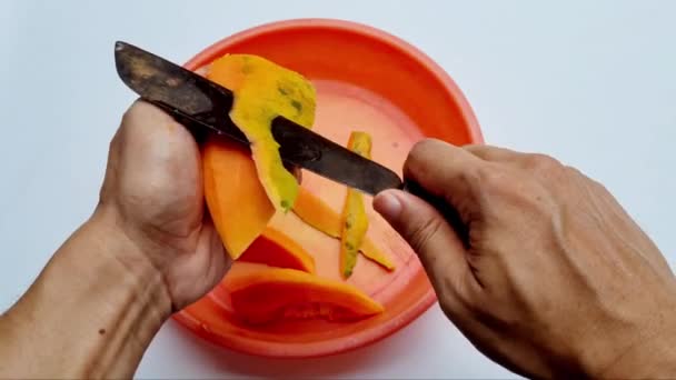 Ruch dłoni młodego człowieka złuszczanie i cięcie dojrzałej papai nożem - Materiał filmowy, wideo