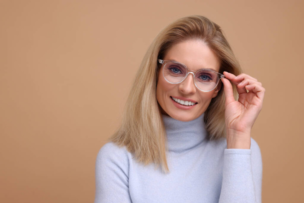 Portrait of smiling middle aged woman in glasses on beige background. Space for text - Photo, image