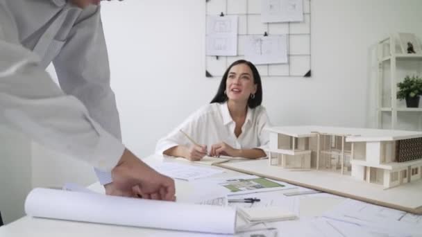 Geschoolde Kaukasische interieurontwerper werkt met huismodel tijdens het bespreken met Aziatische architect ingenieur over huisplan op vergadertafel met blauwdruk en huis model scatter rond. Onbevlekt. - Video