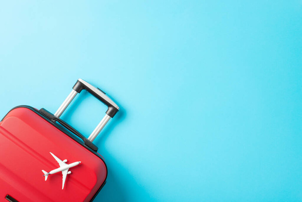 Ready for New Year 's Getaway: Foto von oben mit rotem Koffer und Miniaturflugzeug vor leuchtend blauem Hintergrund mit Werbefläche - Foto, Bild