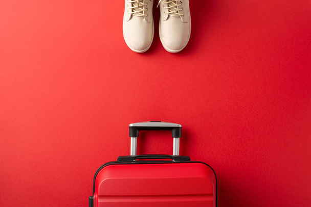 Una idea de escapada de Navidad. Foto aérea de botas de invierno de mujer blanca, que significa el camino a unas vacaciones de invierno, y una maleta en un telón de fondo rojo, con espacio para su mensaje - Foto, imagen