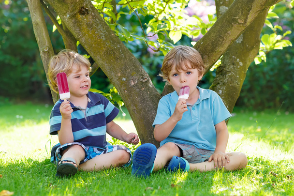 dwóch chłopców rodzeństwo jedzenie czerwonego lody w domu jest ogród. - Zdjęcie, obraz
