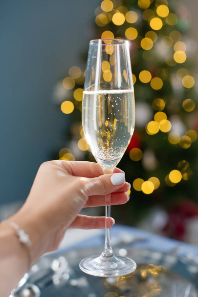 Woman holds glass of champagne on a Christmas tree lights background. New year eve concept - Foto, immagini