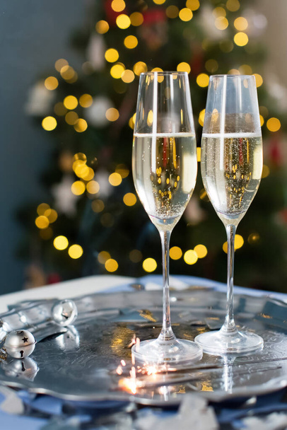 Vintage silver tray with glasses of champagne, christmas bells, burning sparklers and silver confetti on a Christmas tree background - Zdjęcie, obraz