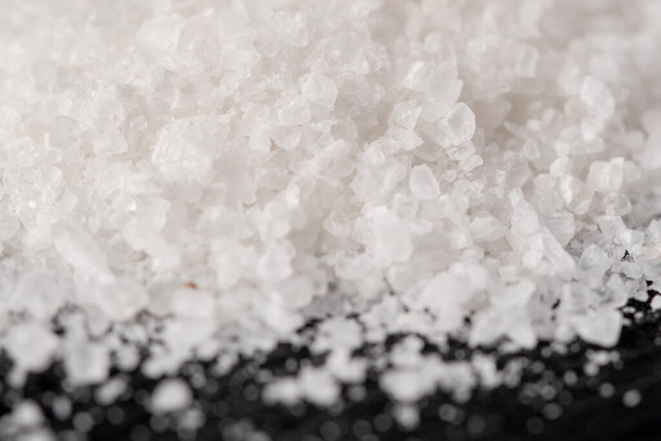 Un montón de cristales de sal blanca sobre un fondo de piedra negra. Comida - Foto, imagen