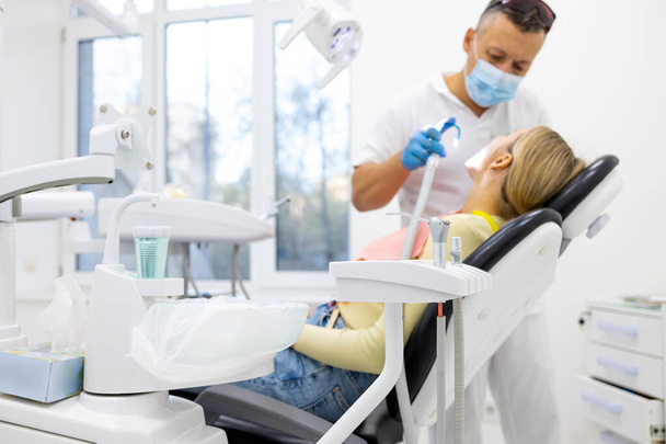 Odontólogo masculino tratando dientes a paciente joven en clínica. Control dental.
. - Foto, Imagen