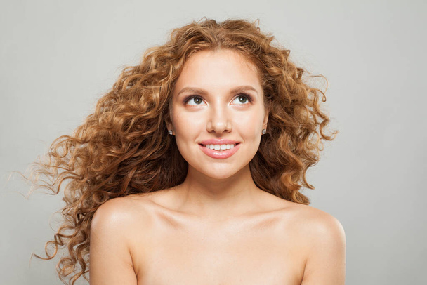 Schöne glückliche Frau mit langen natürlichen gesunden braunen lockigen Haaren und süßem Lächeln, das auf weißem Hintergrund aufblickt. Haarpflege, Haarbehandlung, Wellness und Kosmetologie-Konzept - Foto, Bild