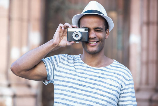 Przystojny mężczyzna trzyma aparat fotograficzny i uśmiecha się podczas spaceru po mieście - Zdjęcie, obraz