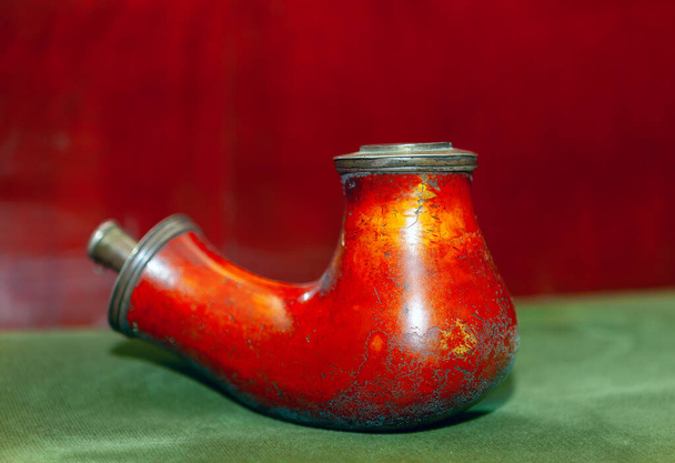 赤い背景の緑のテーブルクロスの古い喫煙パイプ. 何年もの使用によって天候にさらされる煙のためのパイプ - 写真・画像
