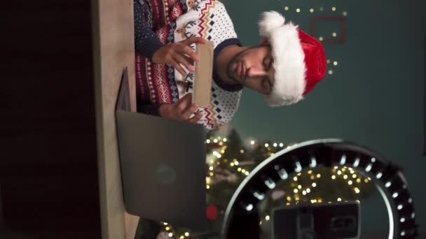 Giovane musulmano blogger maschile disimballaggio scatole regalo regali di Natale e fare live streaming. ragazzo arabo utilizzando fotocamera smartphone per la creazione di contenuti per il suo blog di tecnologia. Video verticale - Filmati, video