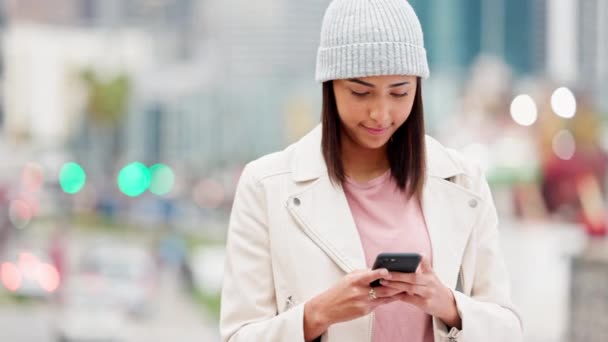 Kobieta śmiejąca się podczas czytania śmiesznego smsa na telefonie w zimny dzień w miejskim mieście. Modna i wesoła kobieta wysyłając wiadomość lub za pomocą przenośnej aplikacji mobilnej, aby zarezerwować taksówkę podczas podróży. - Materiał filmowy, wideo