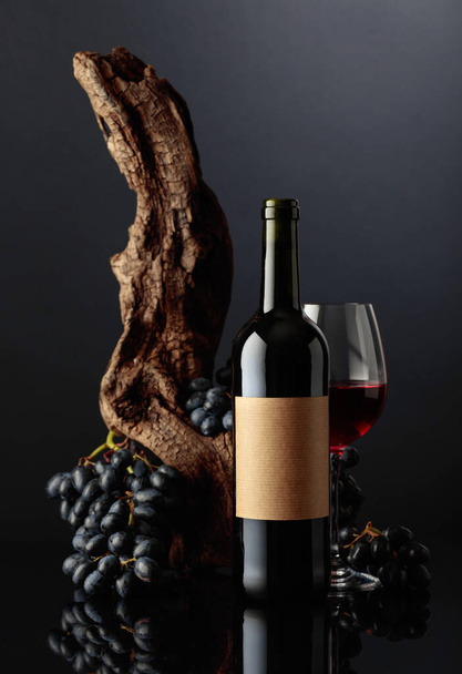 Egy üveg vörösbor régi üres címkével. A háttérben régi viharvert snag és kék szőlő. - Fotó, kép