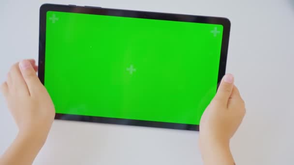 Close-up handen kind vasthouden en tikken op een tablet computer met een horizontaal groen scherm. Zwijg..  - Video
