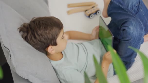 Közelkép gyerek ül a kanapén, billenő balra és jobbra egy tabletta egy vízszintes zöld képernyőn. Krómkulcs. Felülnézet - Felvétel, videó