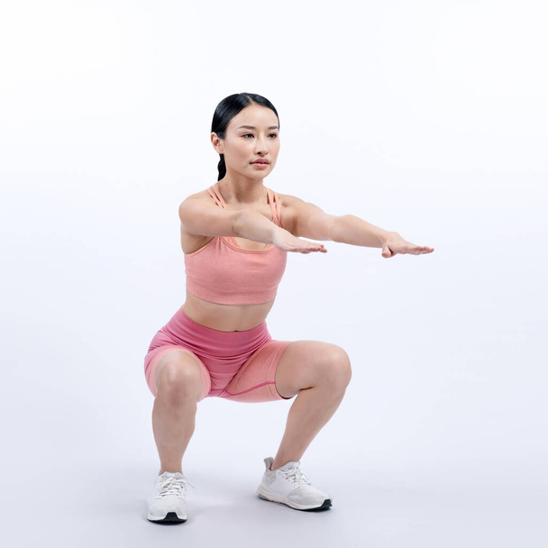 Krachtige energieke vrouw doet aan lichaamsbeweging. Jonge atletische Aziatische vrouw kracht en uithoudingsvermogen training sessie als squat workout routine sessie. Full body studio shot op geïsoleerde achtergrond. - Foto, afbeelding