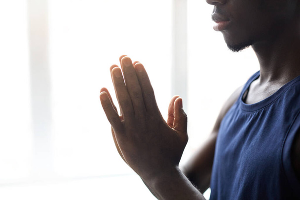 Close-up van Afrikaanse jongeman die zijn handen vouwt en zich concentreert op meditatie tijdens yoga - Foto, afbeelding