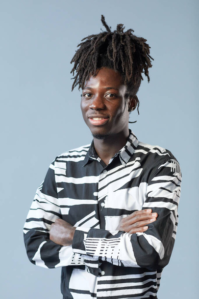 Ritratto di ragazzo africano con acconciatura alla moda in piedi con le braccia incrociate e sorridente alla macchina fotografica su sfondo blu - Foto, immagini