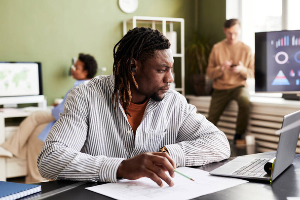 Африканский архитектор смотрит на монитор ноутбука и рисует чертежи на своем рабочем месте - Фото, изображение