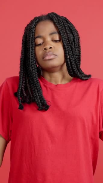 Surullinen afrikkalainen nainen seisoo ja katselee kameraa studiossa punaisella taustalla - Materiaali, video