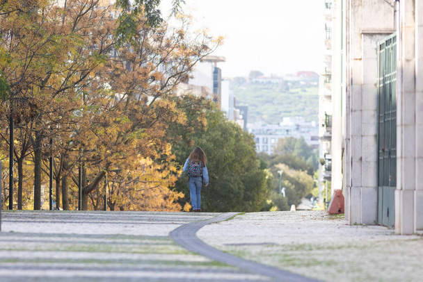 Μια γυναίκα που περπατάει στο δρόμο δίπλα σε ψηλά κτίρια. - Φωτογραφία, εικόνα