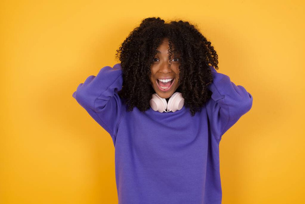 retrato de jovem mulher afro-americana expressiva com fones de ouvido em fundo amarelo - Foto, Imagem