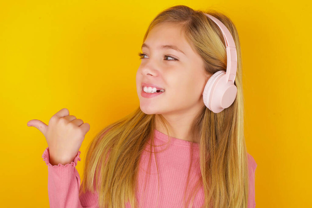 красива дівчина-підліток слухає аудіо доріжку через бездротові навушники вказує на великий палець реклами копіювання простору - Фото, зображення