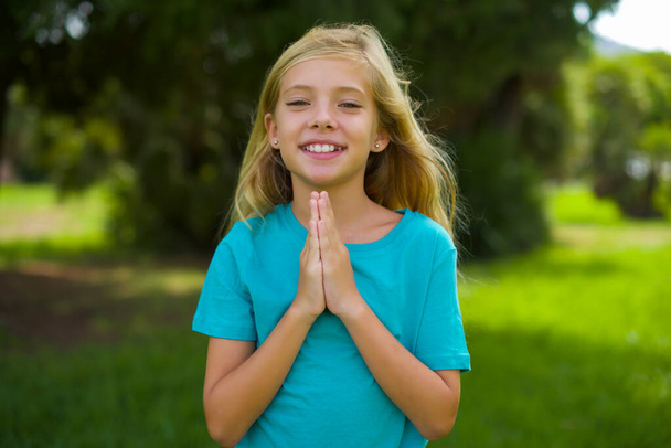 retrato de bela menina caucasiana criança vestindo camiseta azul em pé ao ar livre no parque - Foto, Imagem