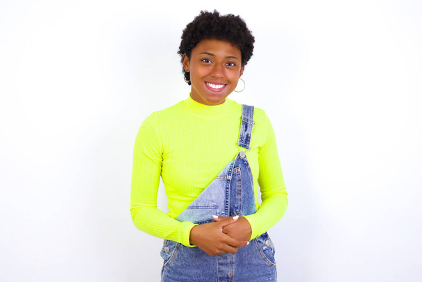 Business Concept - Retrato de una joven afroamericana con el pelo corto usando denim en general contra la pared blanca tomados de la mano con la cara segura. - Foto, imagen