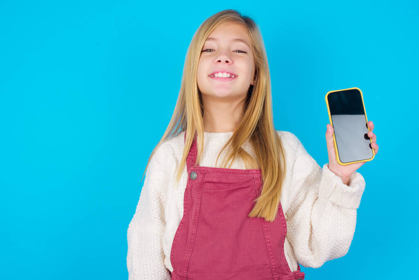 Lächelndes hübsches Teenie-Mädchen mit leerem Telefonbildschirm. Werbe- und Kommunikationskonzept. - Foto, Bild