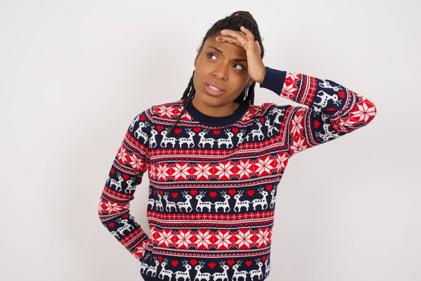 Африканська американка, одягнена в різдвяний светр на білій стіні, що торкається чола, чує щось дивовижне, радий отримувати хороші новини, відчуває полегшення. Майже потрапили в біду. - Фото, зображення