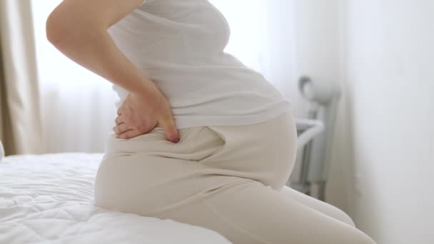 Mujer embarazada en el dormitorio experimenta dolor en el cuerpo. Señora con determinación mece el cuerpo en círculos aliviando de molestias persistentes cuerpo de la cosecha - Metraje, vídeo