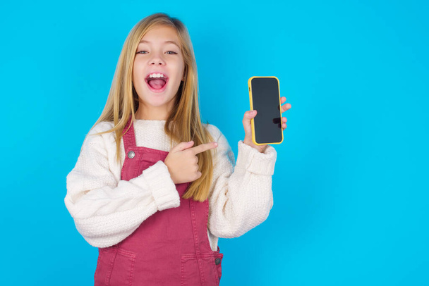 Захоплена красива дівчина тримає і вказує пальцем на смартфон з порожнім екраном. Концепція реклами. - Фото, зображення