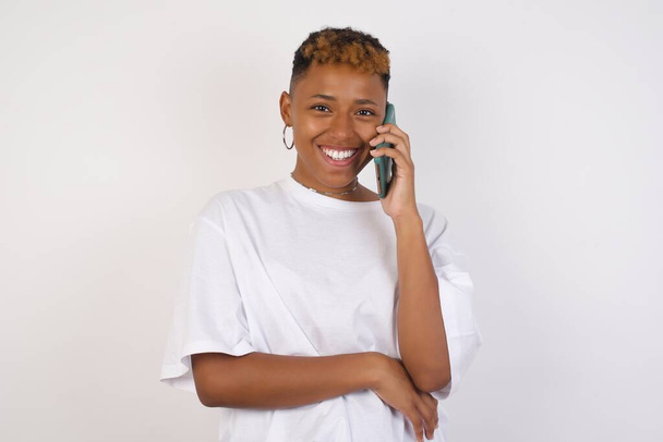 Portrait of a smiling young casual black woman talking on mobile phone isolated over white background. - Фото, зображення