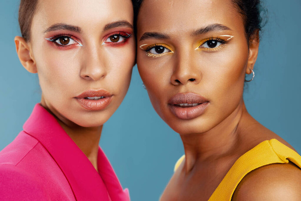 Femme mixte américain modèle maquillage caucasien deux africaine jaune soins ensemble briller coloré attrayant studio sain oeil portrait heureux fille peau race beauté soins du corps beau visage - Photo, image