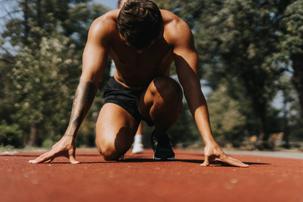 Sport férfi személy kezdő futópozícióban, felkészülés futtatni egy versenypályán a parkban egy gyönyörű napsütéses napon. - Fotó, kép