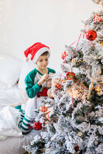 Ritratto di ragazzo allegro che sorride e ride accanto all'albero di Natale a casa. Famiglia e generazione bambini alpha festeggiano le vacanze invernali. - Foto, immagini