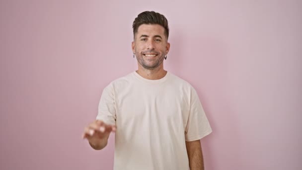 Χαρούμενος νεαρός ισπανόφωνος άνδρας με αυτοπεποίθηση δείχνει μια καλή χειρονομία, στέκεται απομονωμένος σε ένα γαλήνιο ροζ φόντο, ακτινοβολεί θετικότητα, ένα συγκινητικό χαμόγελο, και casual-fashion δροσιά. - Πλάνα, βίντεο