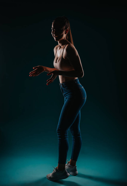 Уверенная в себе девушка позирует в темной студии - фитнес-модель упражнения для трансформации тела с мощными результатами - Фото, изображение